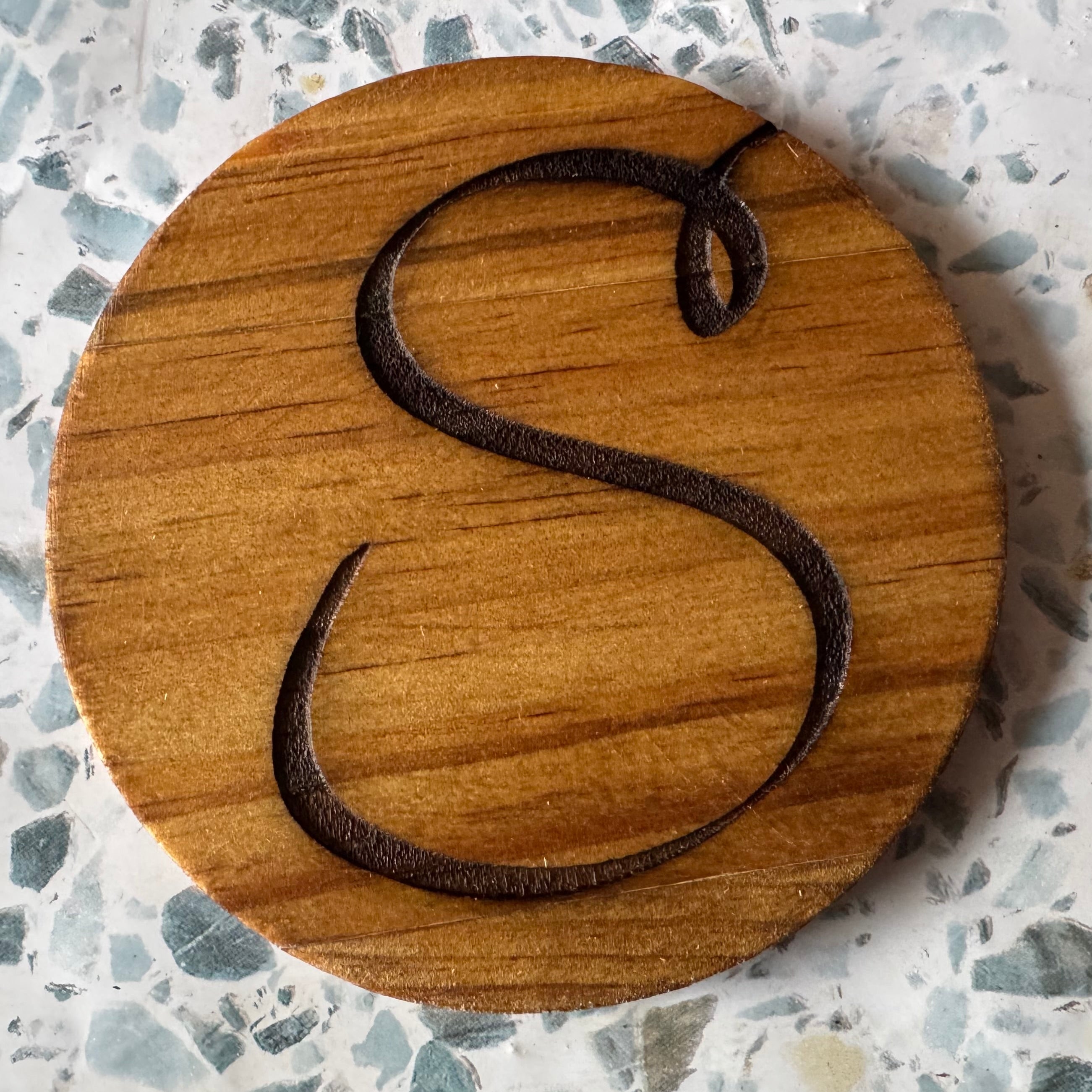 Wooden coaster with letter 'S' on a speckled surface