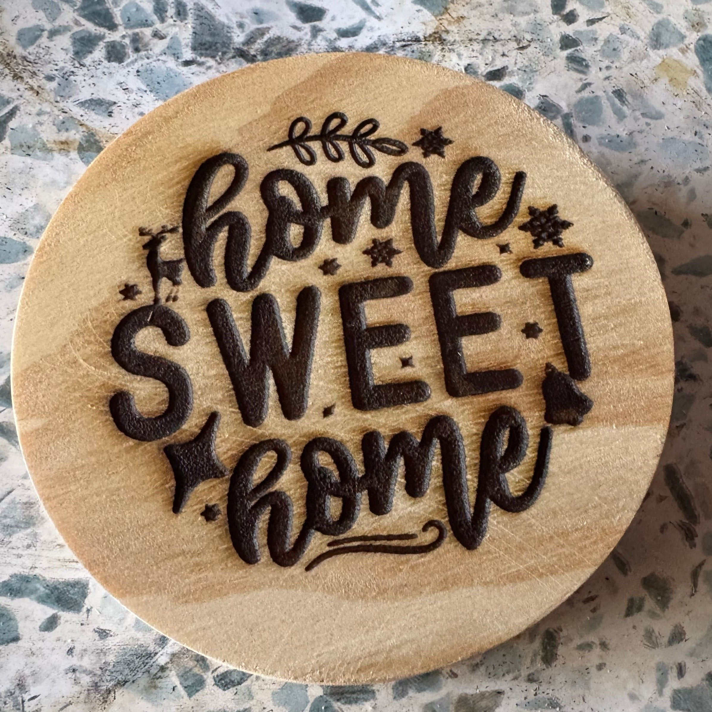 Wooden round coaster with 'home sweet home' engraving on a speckled surface