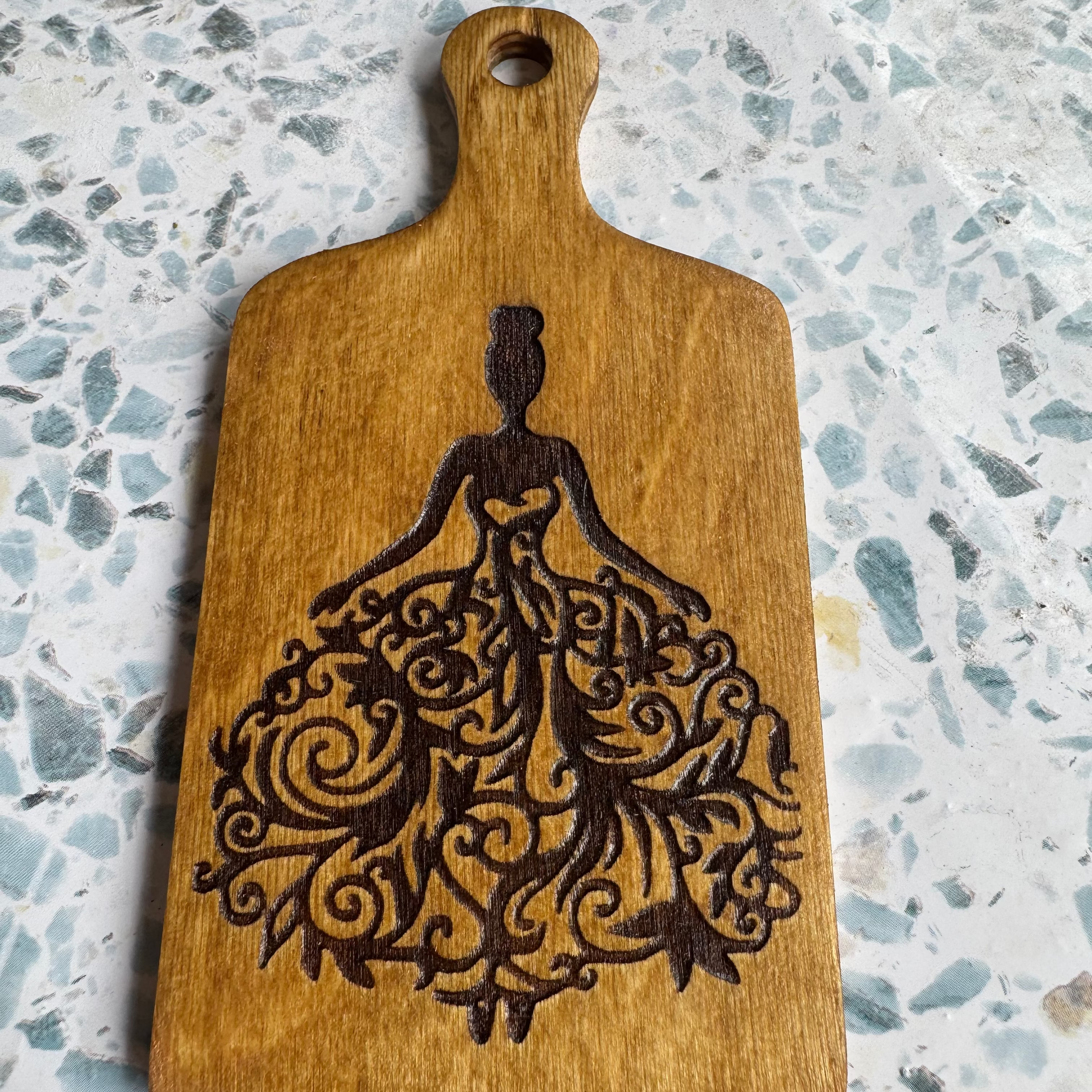 Wooden 6 inch paddle with a decorative cutout design on a speckled countertop