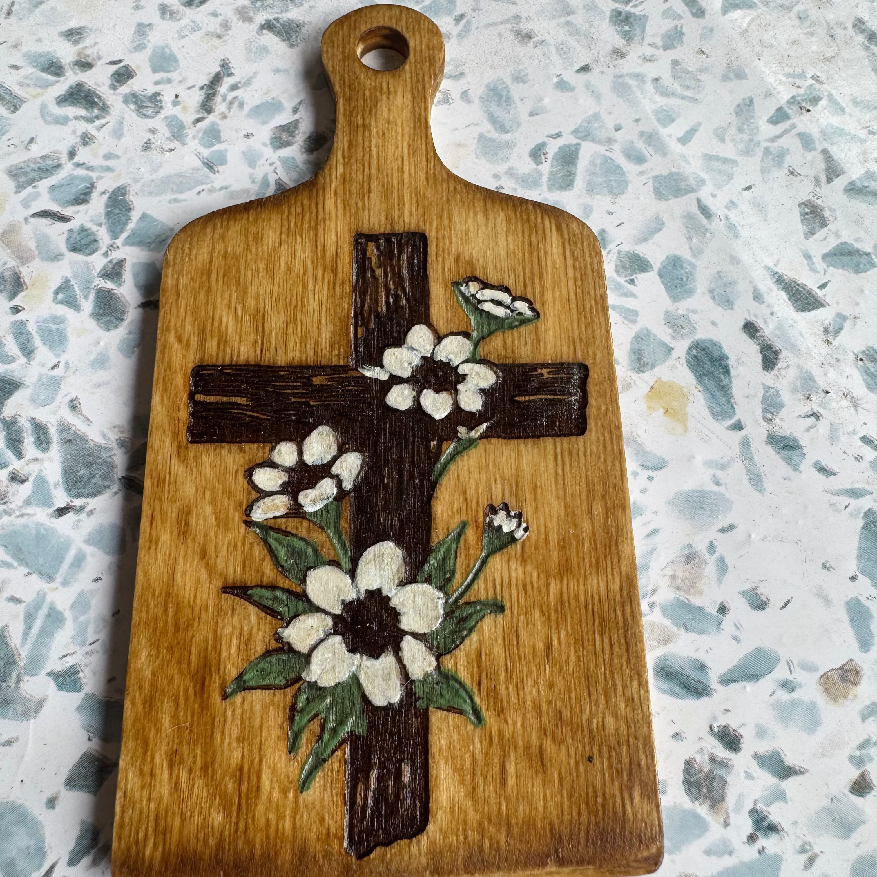 Wooden 6 inch wooden paddle with a cross and floral design on a textured surface