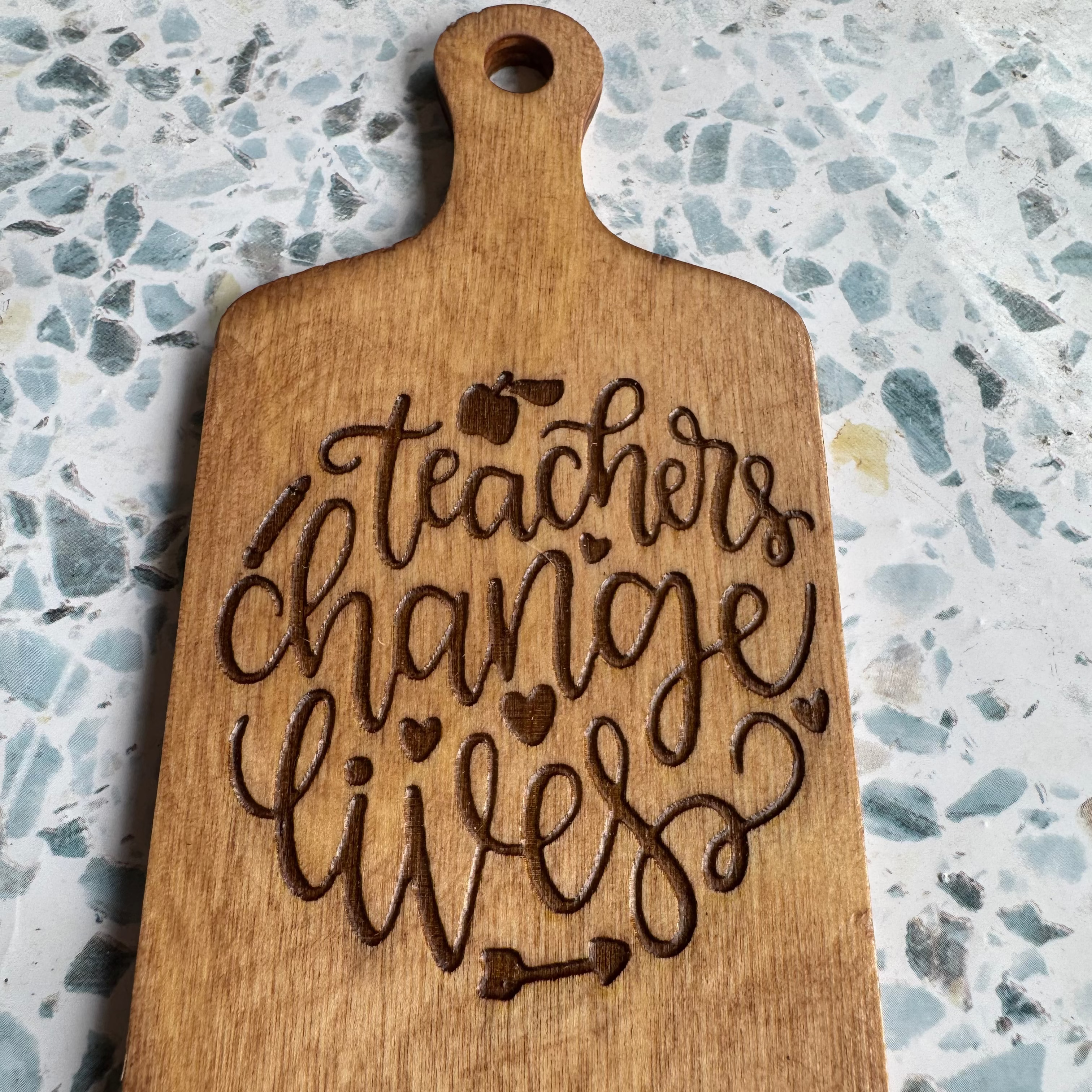 Wooden 6-inch board with 'Teachers change lives' engraving on a speckled countertop.