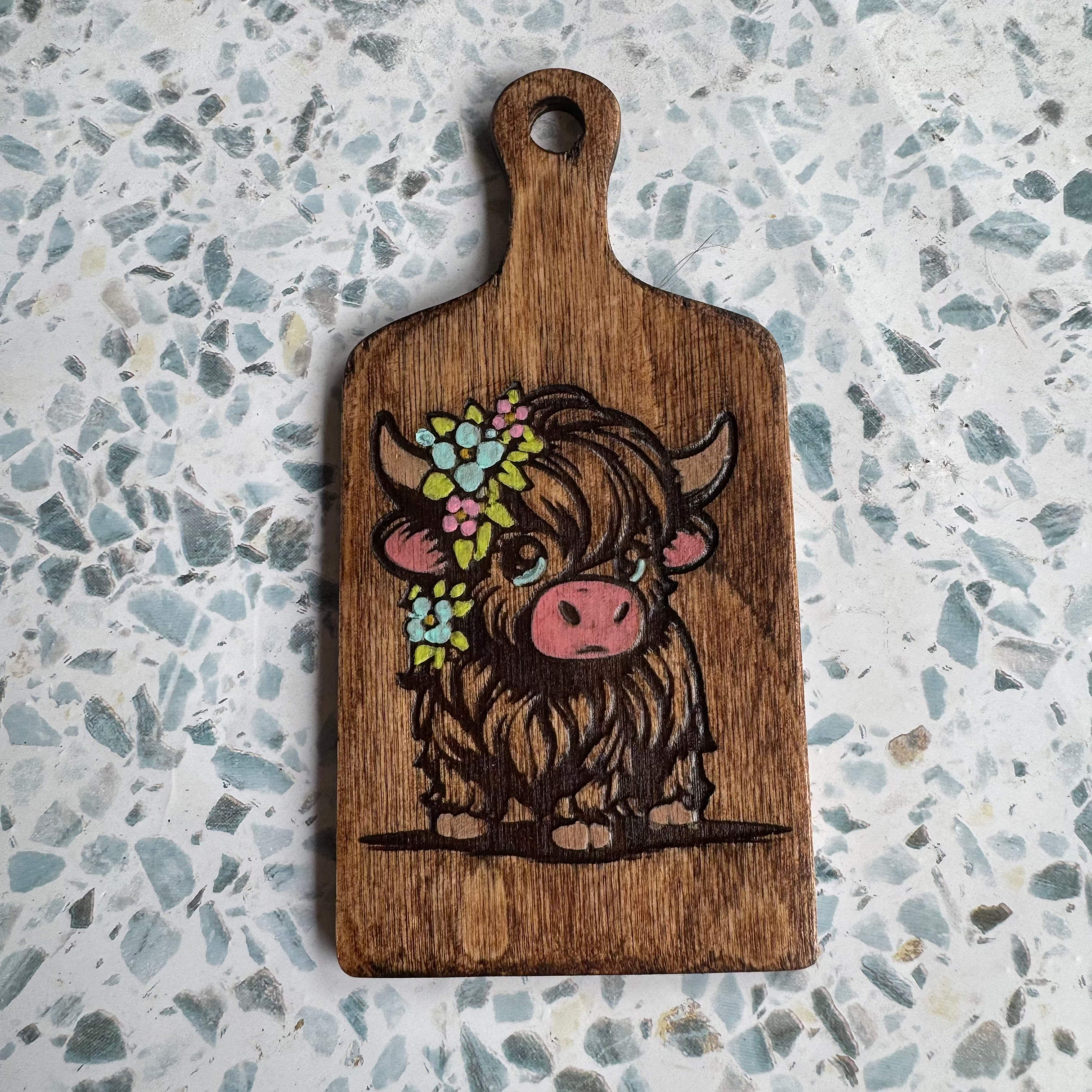 Wooden 6-inch paddle with an engraved cow design on a speckled countertop
